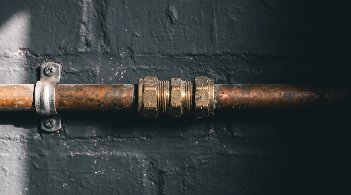 Copper heating pipework clipped to a dark wall with a brass compression fitting